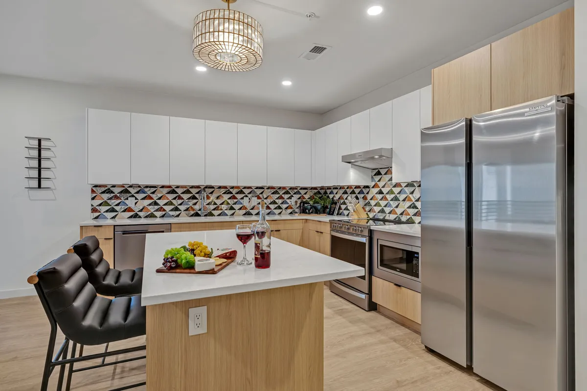A sleek kitchen with a colorful geometric backsplash, a central island with seating, stylish pendant lighting, and stainless steel appliances. The area is designed for both functionality and flair, encouraging culinary creativity and easy socializing.