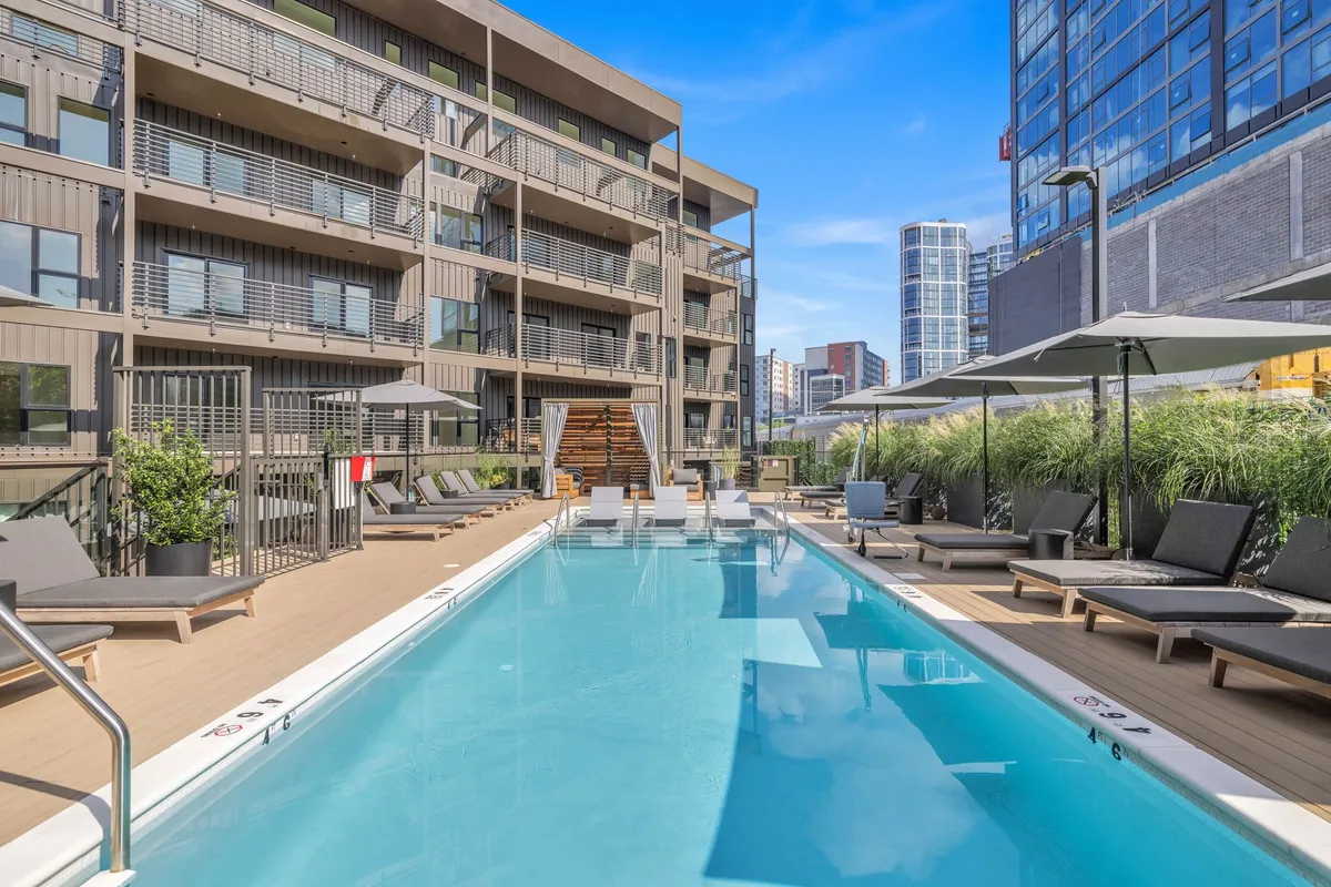 A sparkling swimming pool surrounded by lounge chairs, umbrellas, and landscaping, set against the backdrop of the building’s facade. The scene is lively yet relaxing, with ample space for sunbathing, socializing, or unwinding after a busy day.