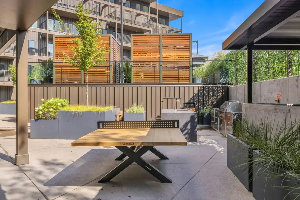 A casual outdoor dining area with a wooden table, planter boxes, and a dedicated grilling station set against warm wooden screens—ideal for barbecues, casual meals, and evening gatherings under the stars.
