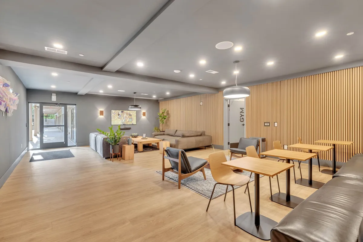 Chic lounge areas with inviting sofas, wooden tables, contemporary decor, and visible access to other amenity spaces such as the gym. The mood is relaxed yet vibrant, suited for socializing, working, or unwinding with friends.