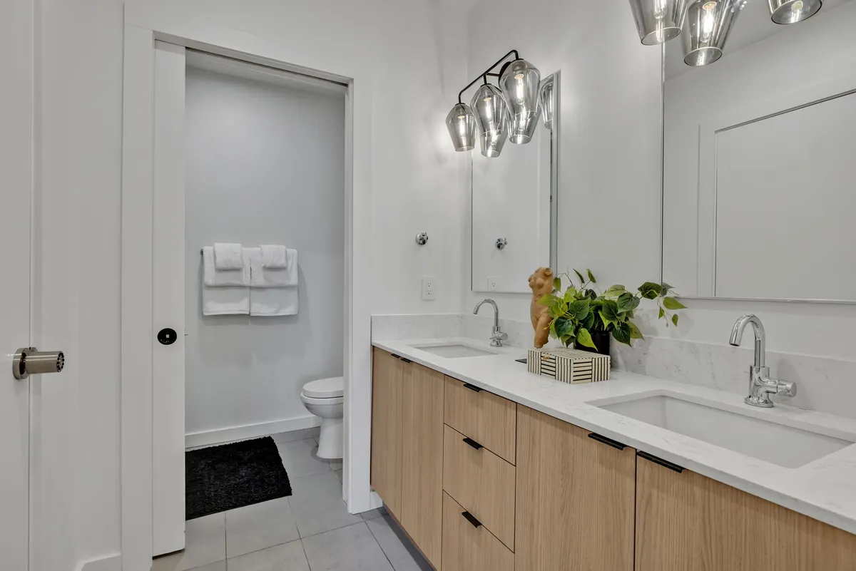 A contemporary bathroom with a double sink vanity, modern light fixtures, indoor plant, and plush towels. The space is bright and airy, inviting guests to unwind and enjoy self-care rituals.