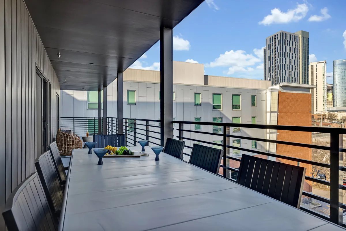 A long outdoor dining table adorned with decorative centerpieces, set against a backdrop of the city skyline. The space suggests communal dining, celebrations, and relaxing al fresco with breathtaking views.